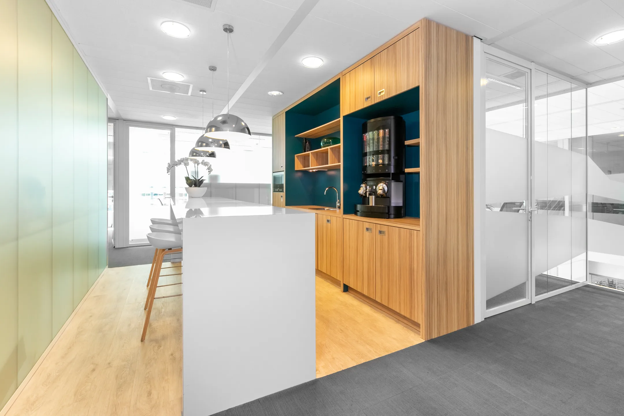 Een moderne kantoorpantry met een houten kast, een koffiezetapparaat, en een lange witte tafel met stoelen.