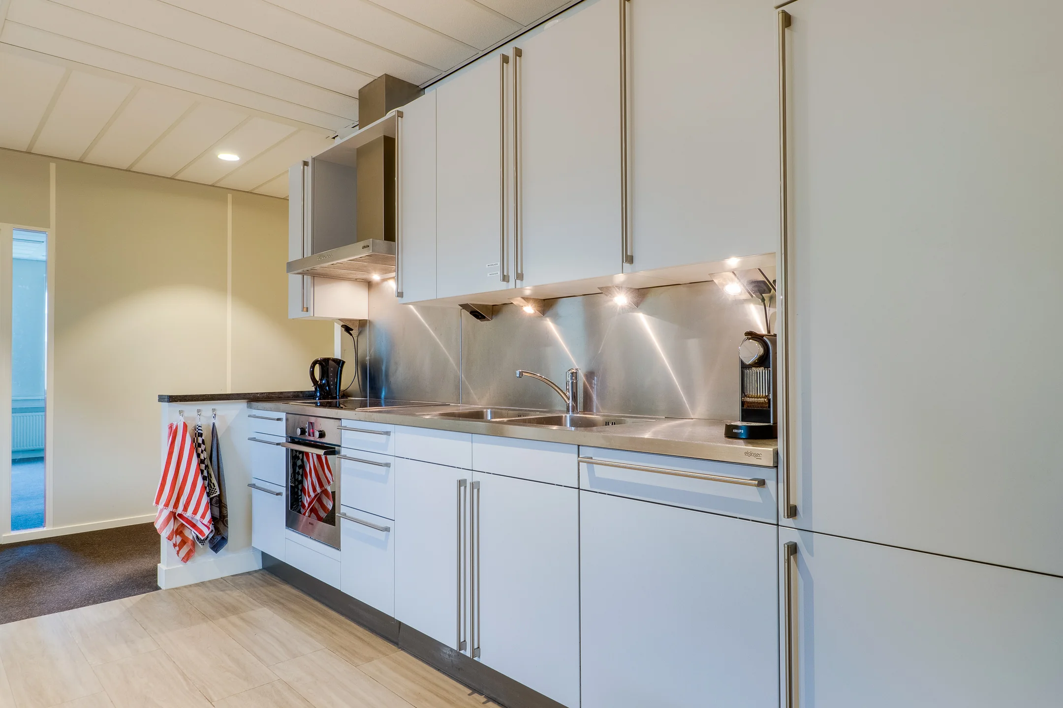 Een moderne keuken met witte kasten, een fornuis, gemonteerd koffiezetapparaat en kleurrijke theedoeken aan de muur.