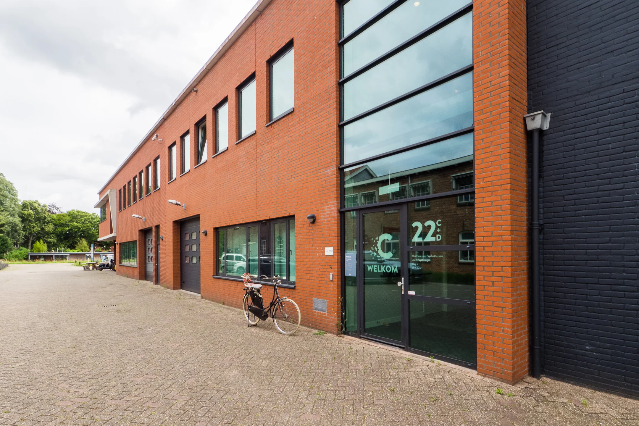 Bakstenen kantoorgebouw met glazen ingang en een fiets naast de deur.