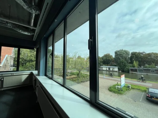 Uitzicht vanuit een raam aan de Kanaalweg met zicht op een fietspad en boten op het water.
