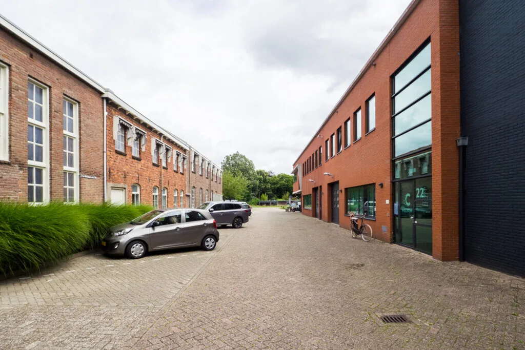 Een rustige straat met geparkeerde auto's tussen twee bakstenen gebouwen aan de Kanaalweg.