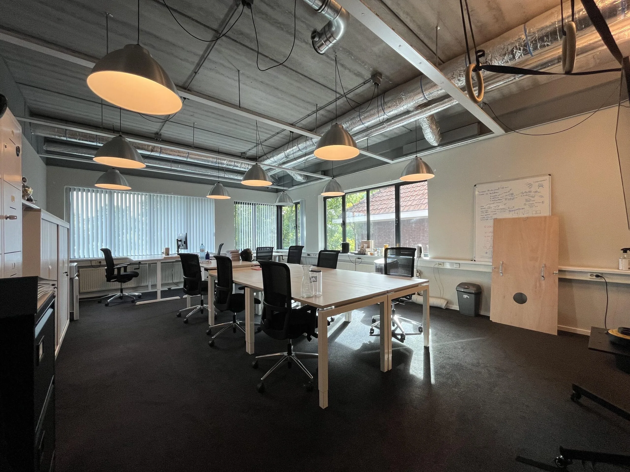 Een moderne vergaderruimte met een grote tafel, meerdere stoelen, hanglampen en een whiteboard.