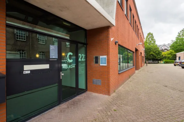 Ingang van een bakstenen gebouw aan de Kanaalweg met glazen deuren en het huisnummer 22B.