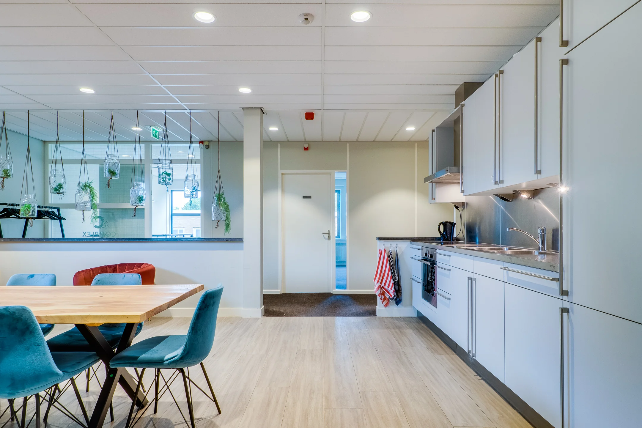 Een moderne keuken met witte kasten en een houten eettafel met kleurrijke stoelen.