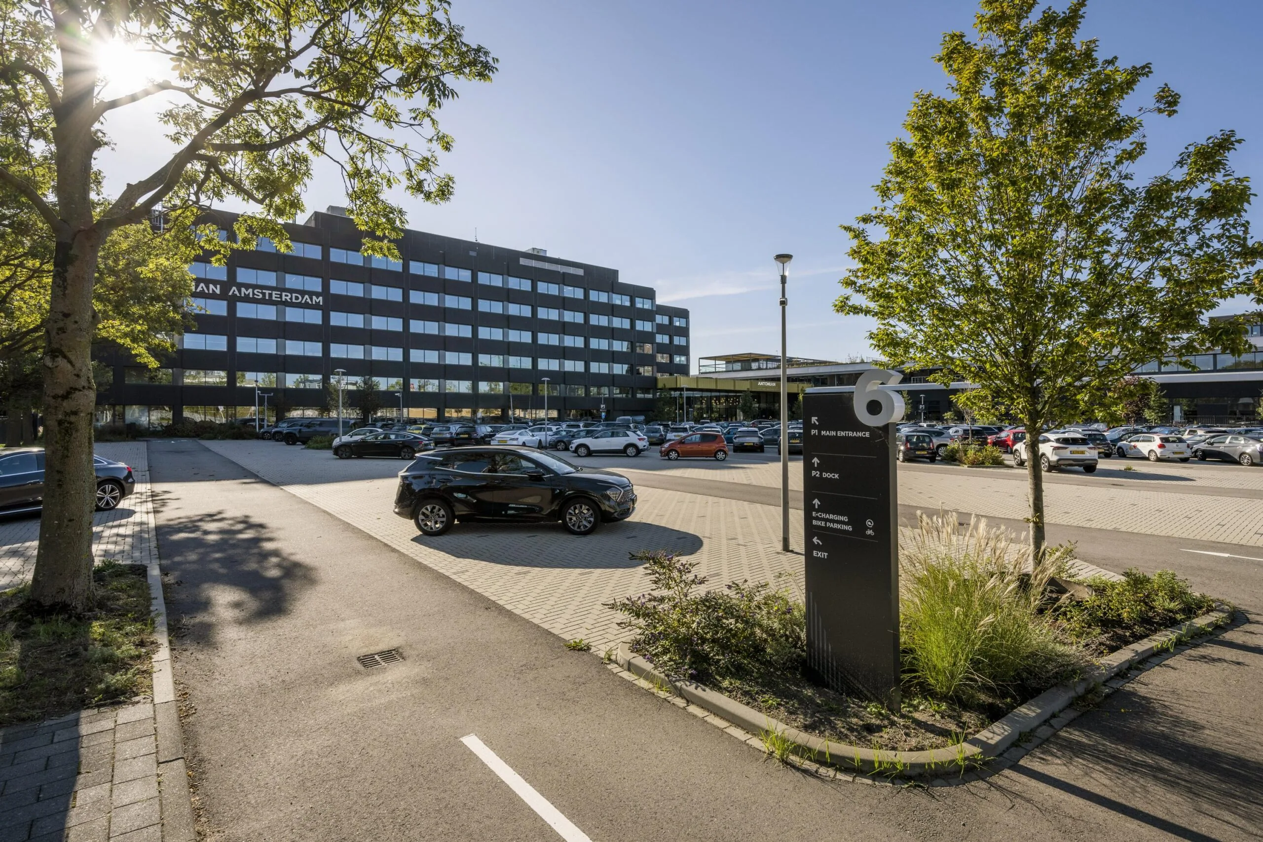 Een parkeerplaats bij een groot gebouw aan de Spaklerweg, met een duidelijk zichtbaar bord voor bezoekers.