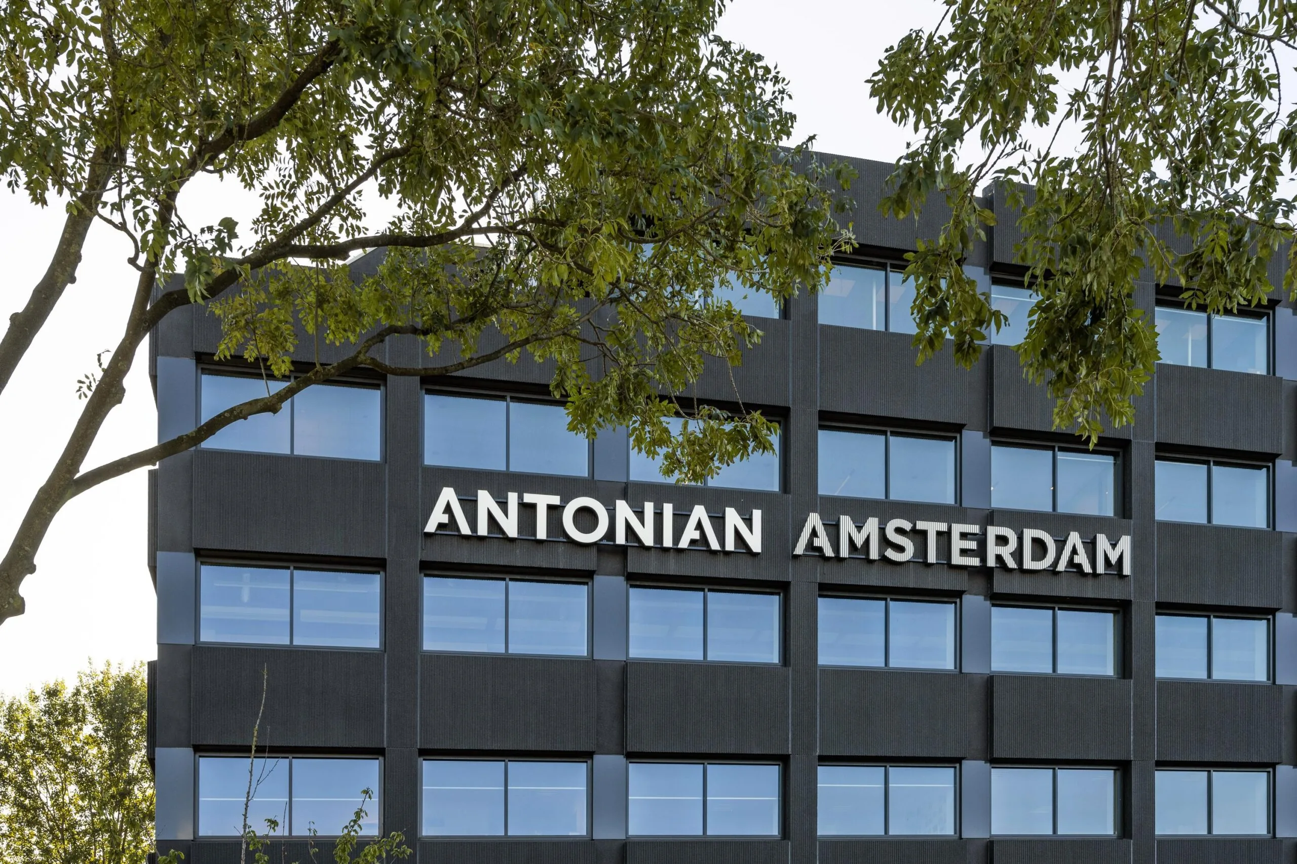 Voorgevel van het gebouw "Antonian Amsterdam" met bomen op de voorgrond.
