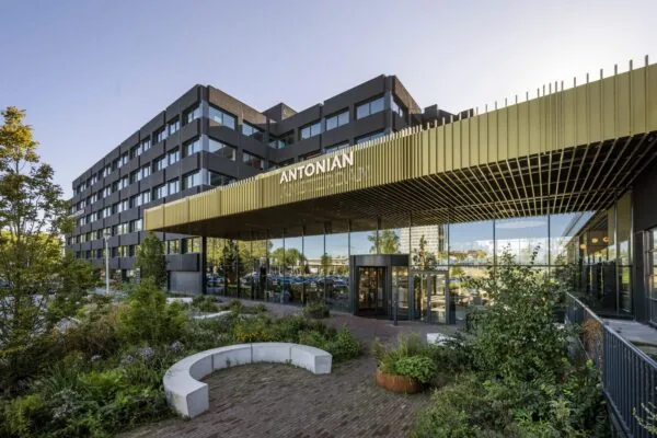 Voorzijde van een modern gebouw aan de Spaklerweg met de naam "ANTONIAN" zichtbaar boven de ingang, omgeven door groene beplanting.