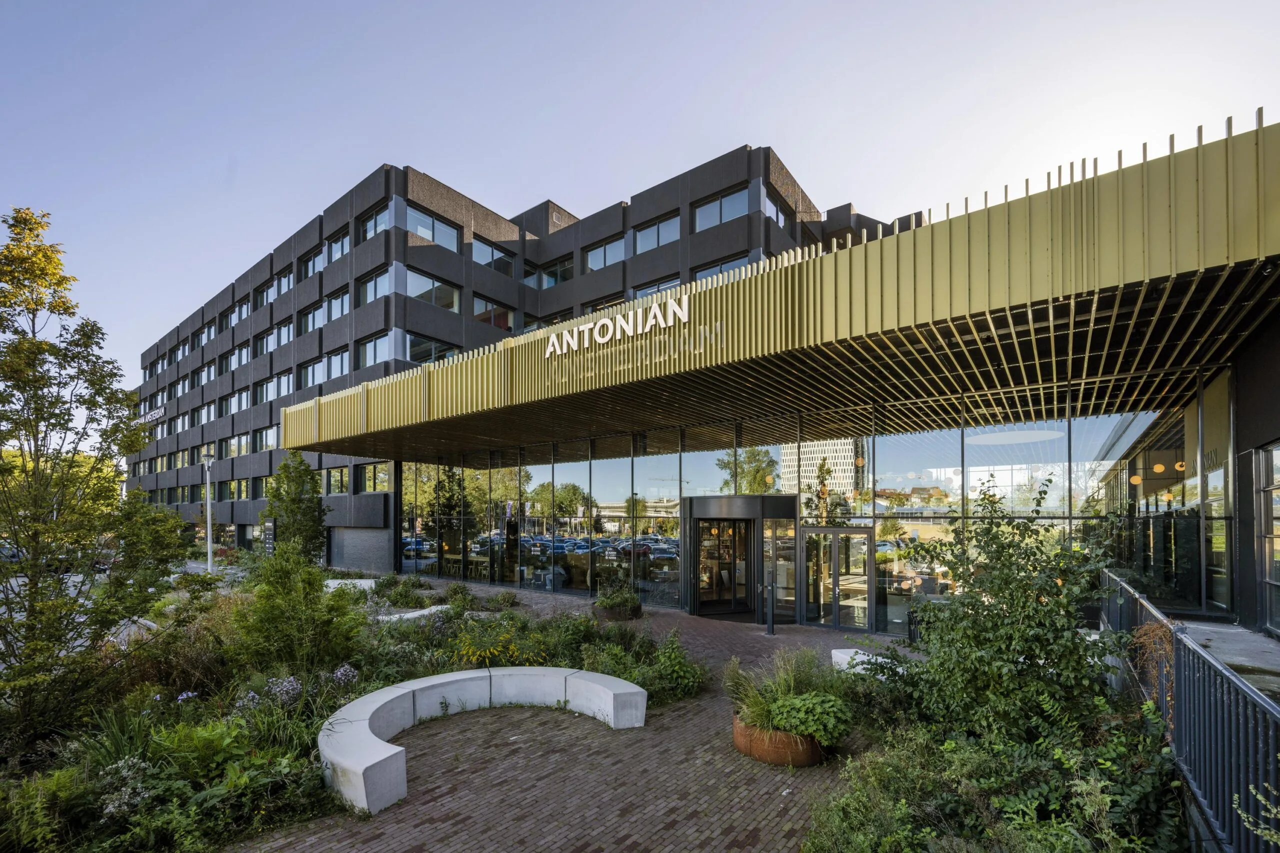 Voorzijde van een modern gebouw aan de Spaklerweg met de naam "ANTONIAN" zichtbaar boven de ingang, omgeven door groene beplanting.