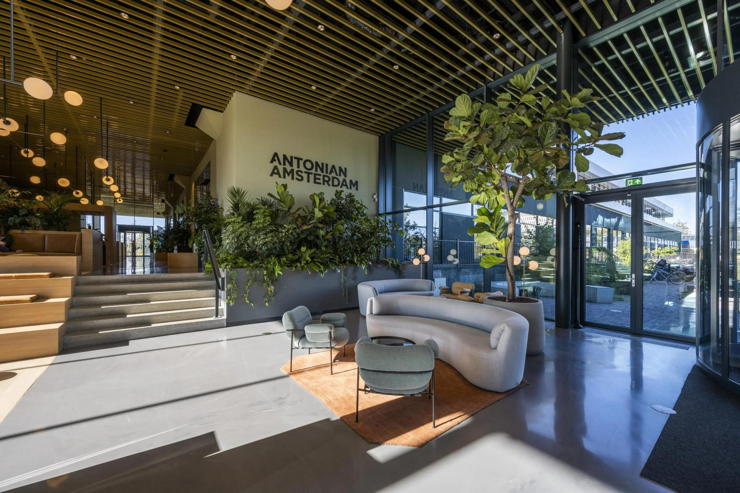 Ingang van het Antonian Amsterdam met moderne inrichting en veel groen.