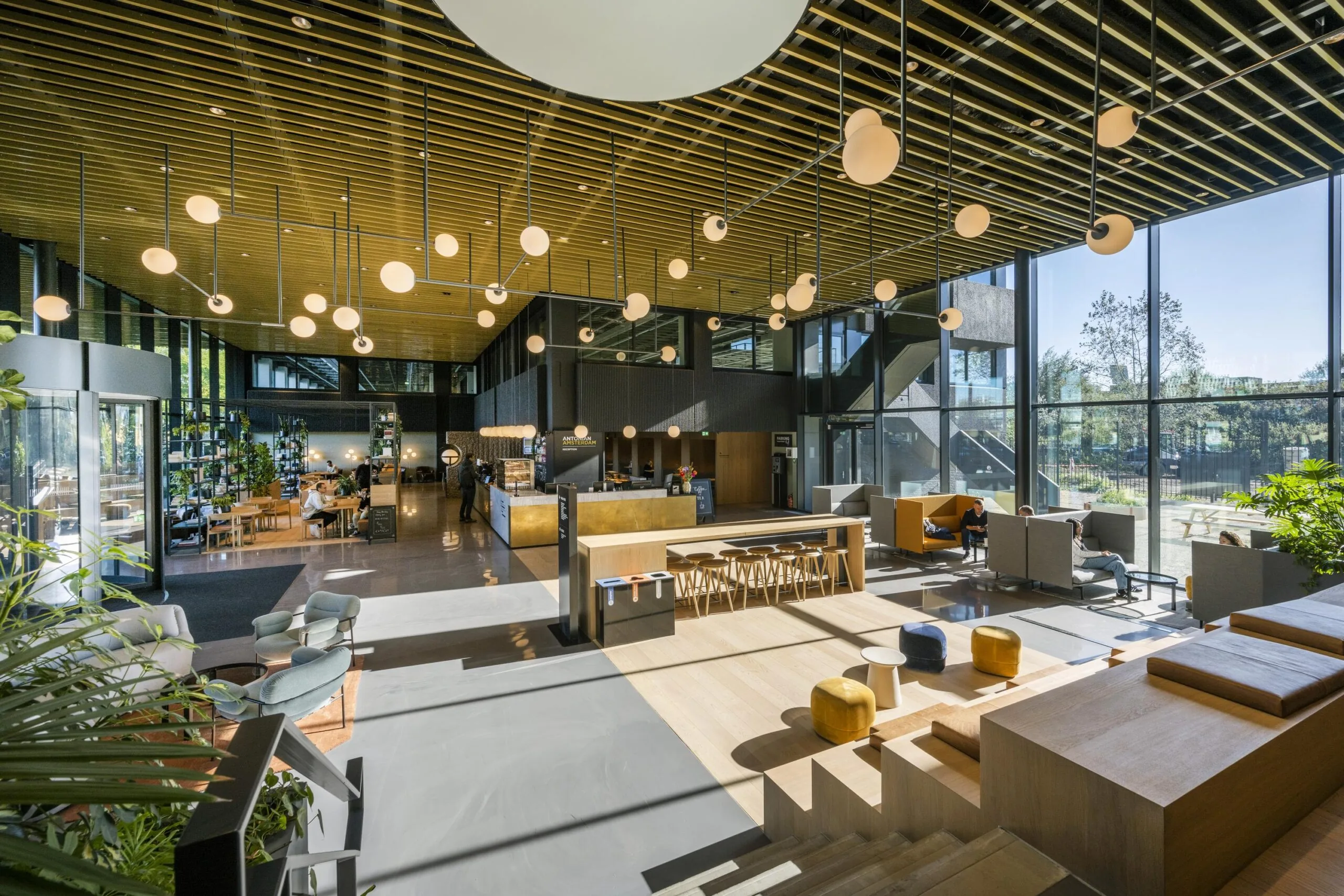 Een moderne en zonnige lobbyruimte met zitgedeelte en decoratieve hanglampen aan het plafond.