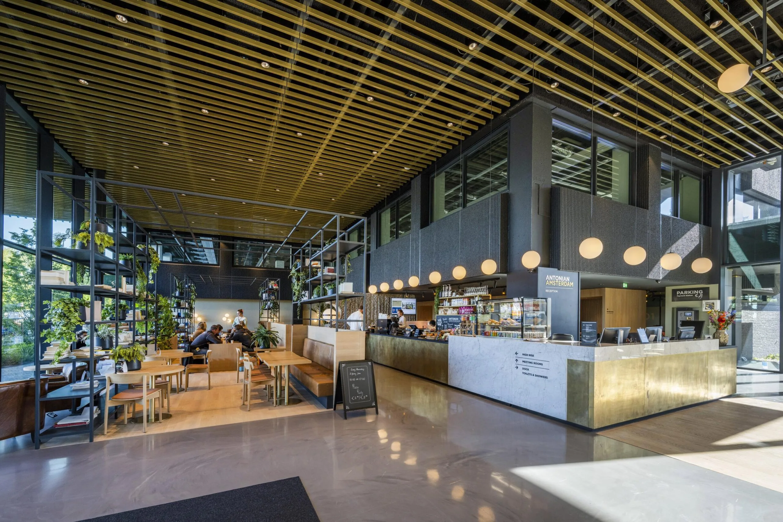Interieur van een moderne lobby met houten plafond, planten en een caféhoek.
