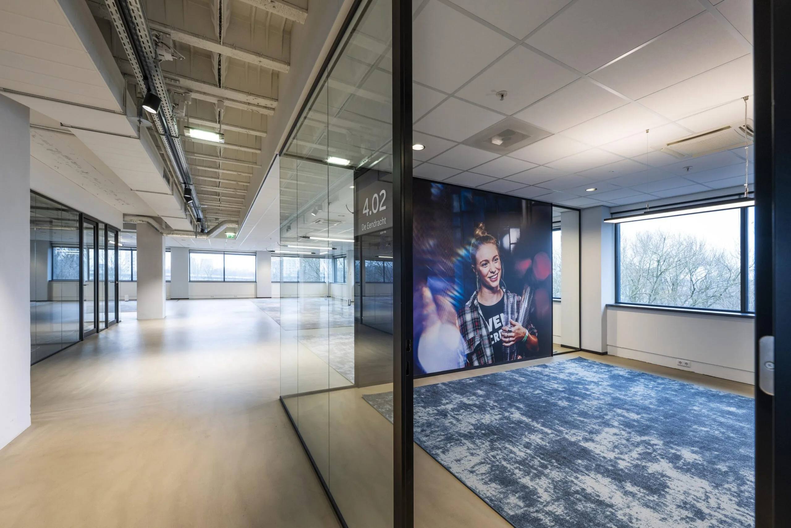 Een moderne kantoorruimte met glazen wanden en een groot fotomuurportret naast vergaderzaal 4.02.
