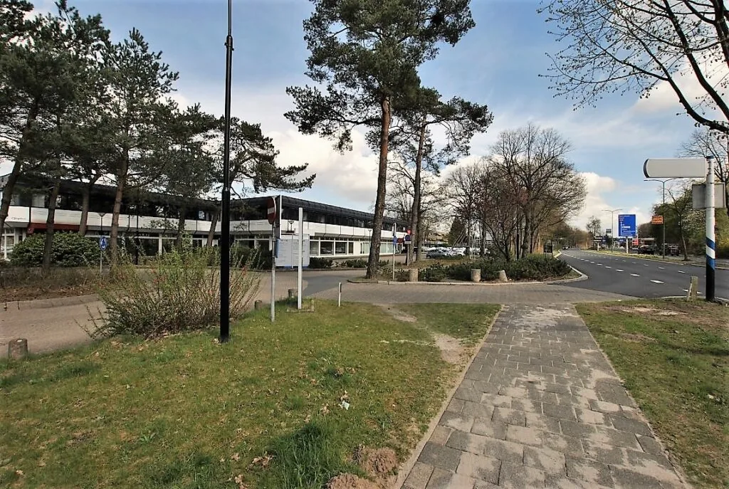 Een weg met bomen en een kantoorgebouw aan de Huis ter Heideweg op de achtergrond.