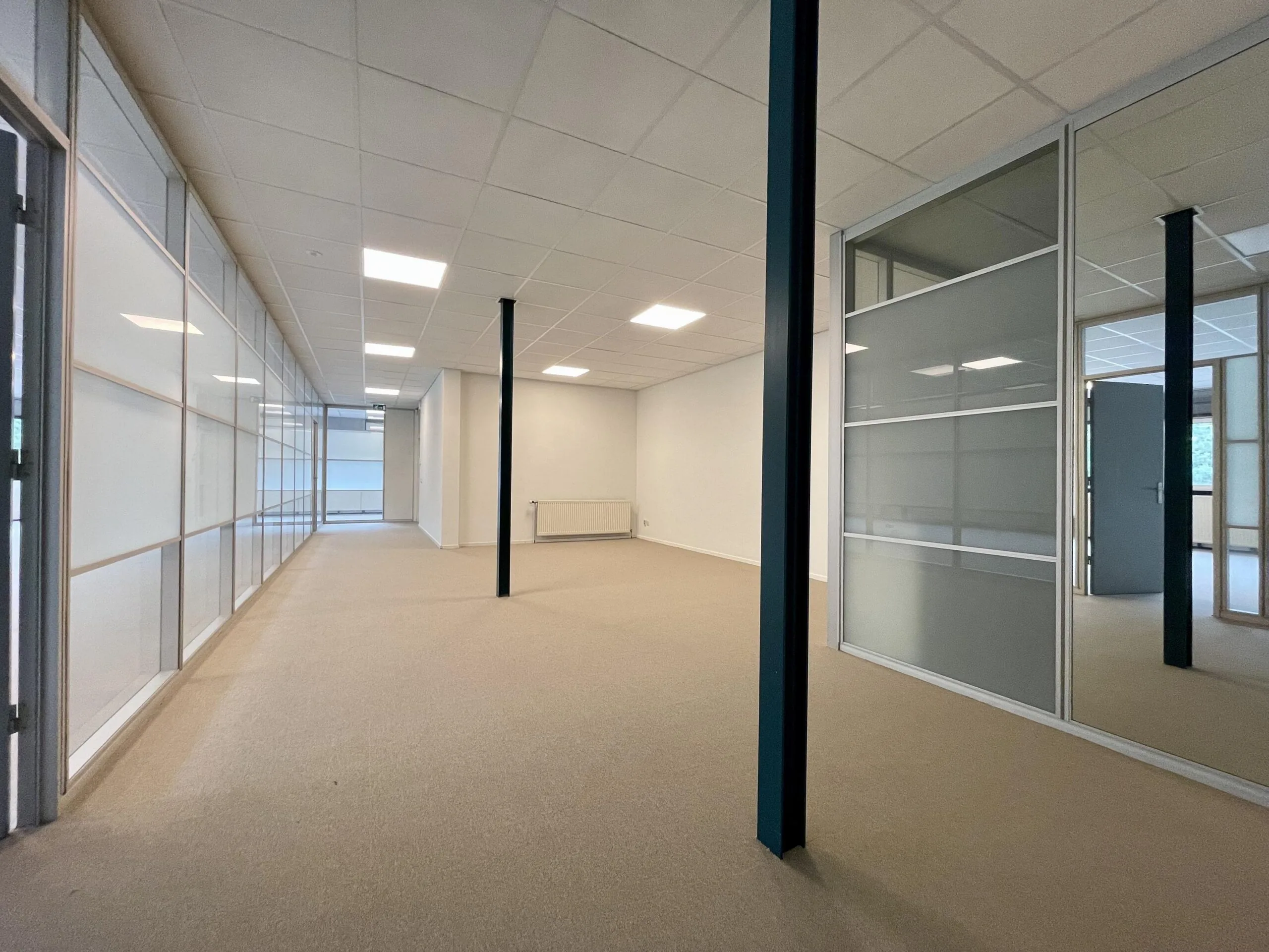 Een lege kantoorruimte met glazen wanden en een lichtkleurig plafond.