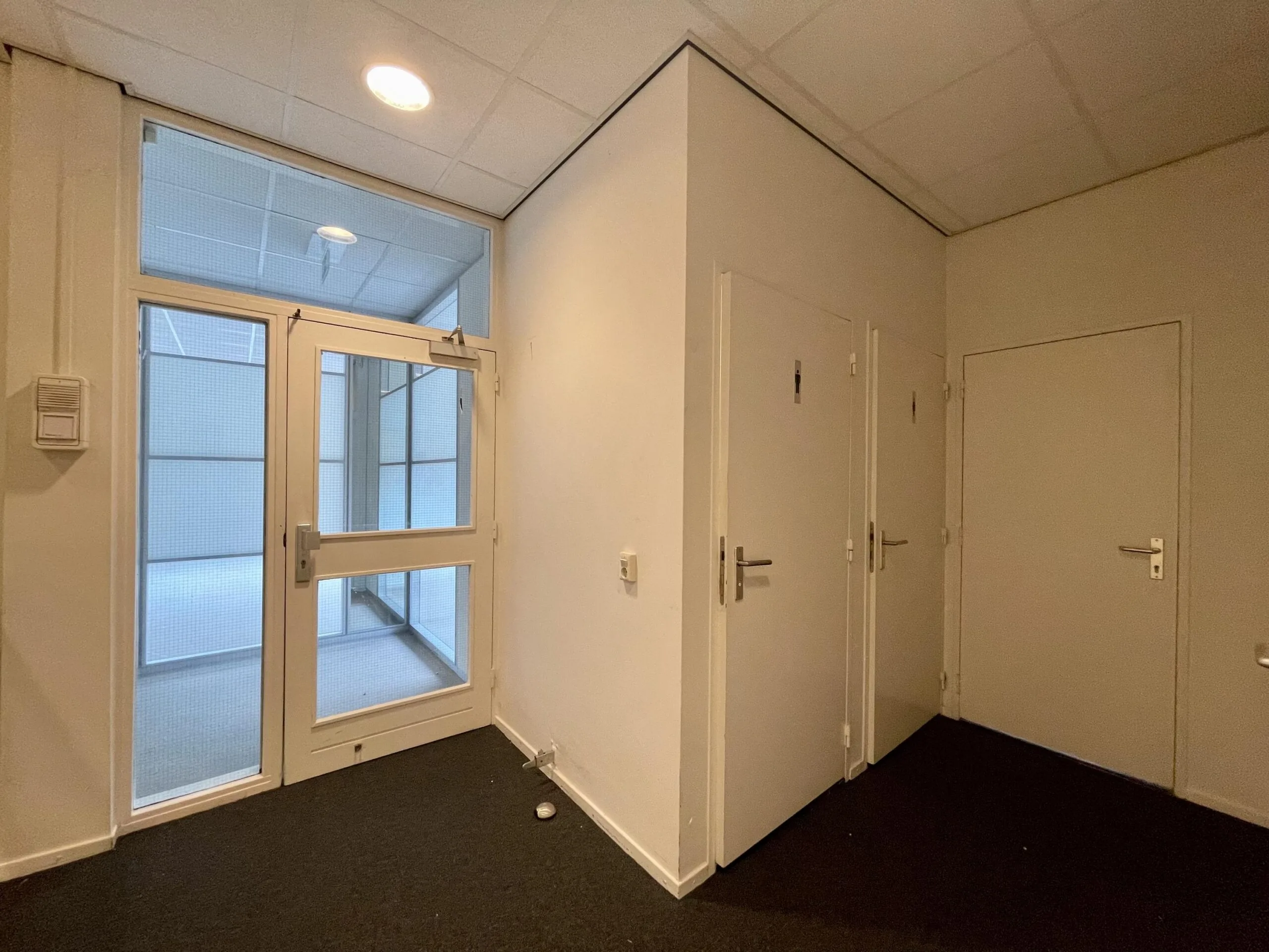 Een kleine hal met drie gesloten deuren en een raamdeur met uitzicht op een overdekte ruimte.