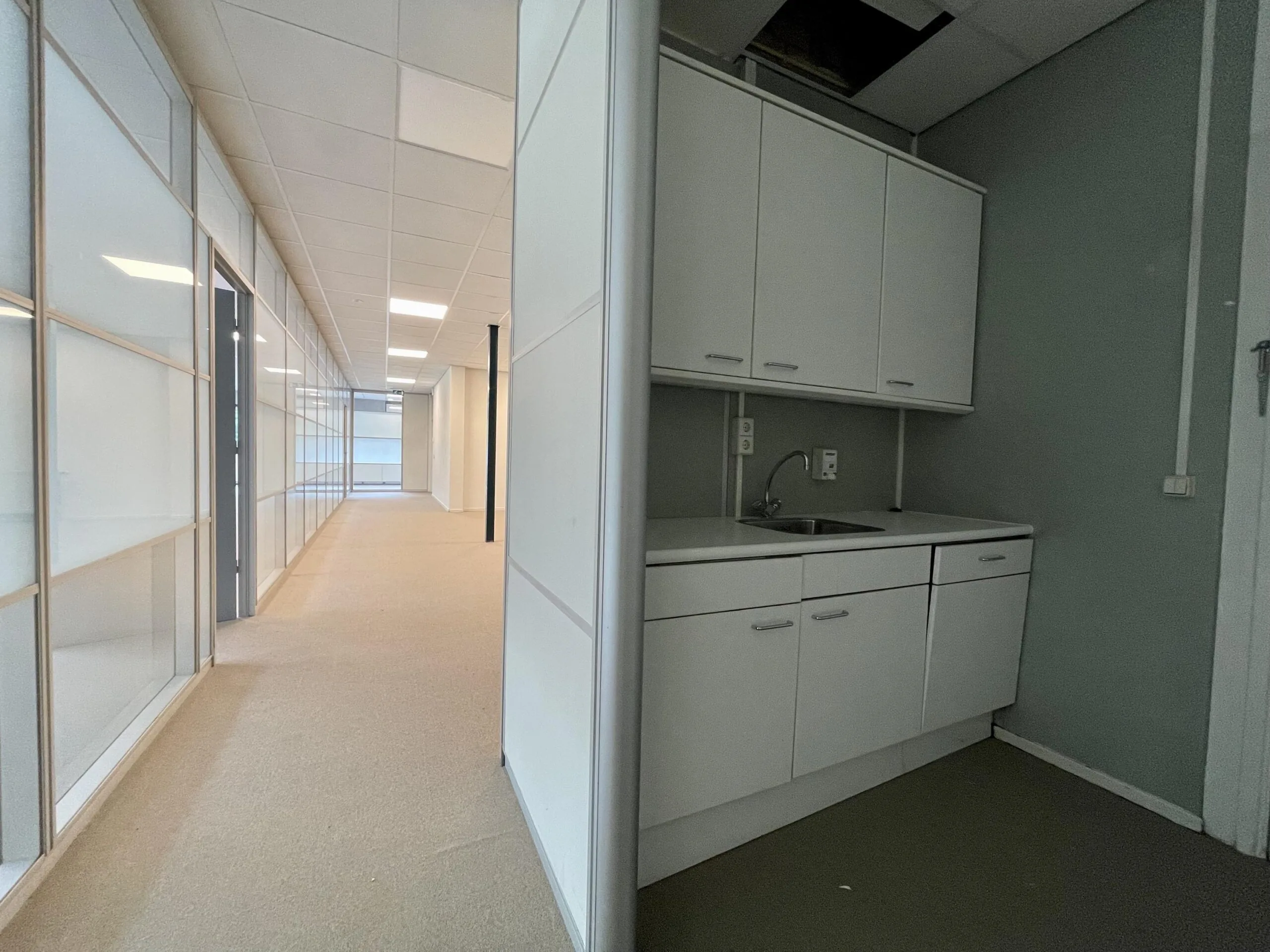 Een moderne kantoorruimte met een lange gang en een kleine kitchenette aan de rechterkant.