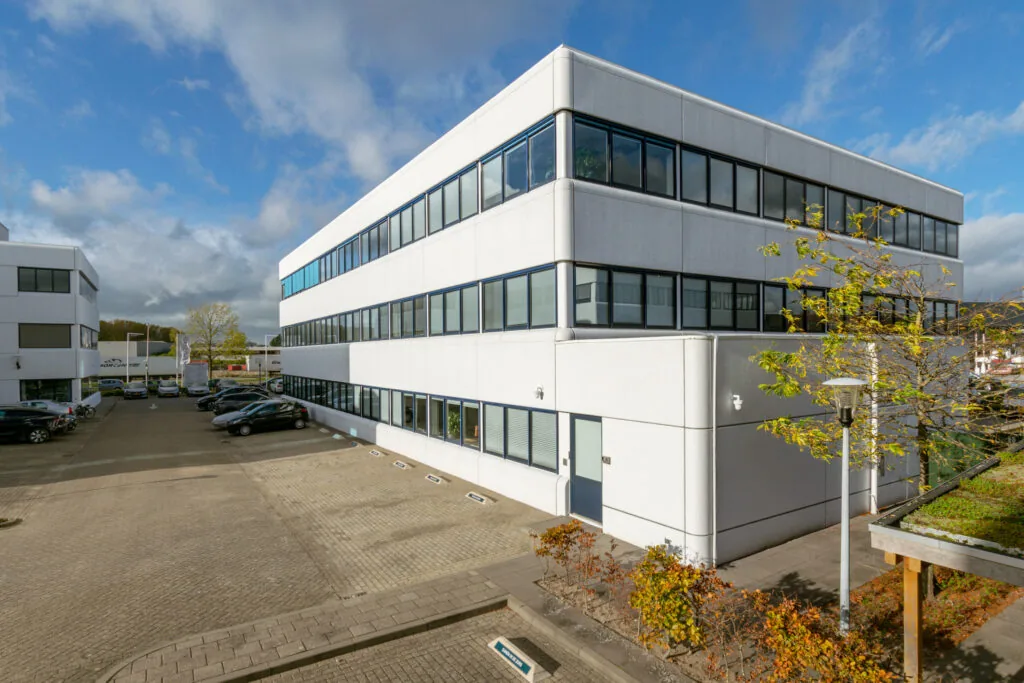 Modern wit kantoorgebouw aan de Atoomweg met parkeerplaatsen en bomen.