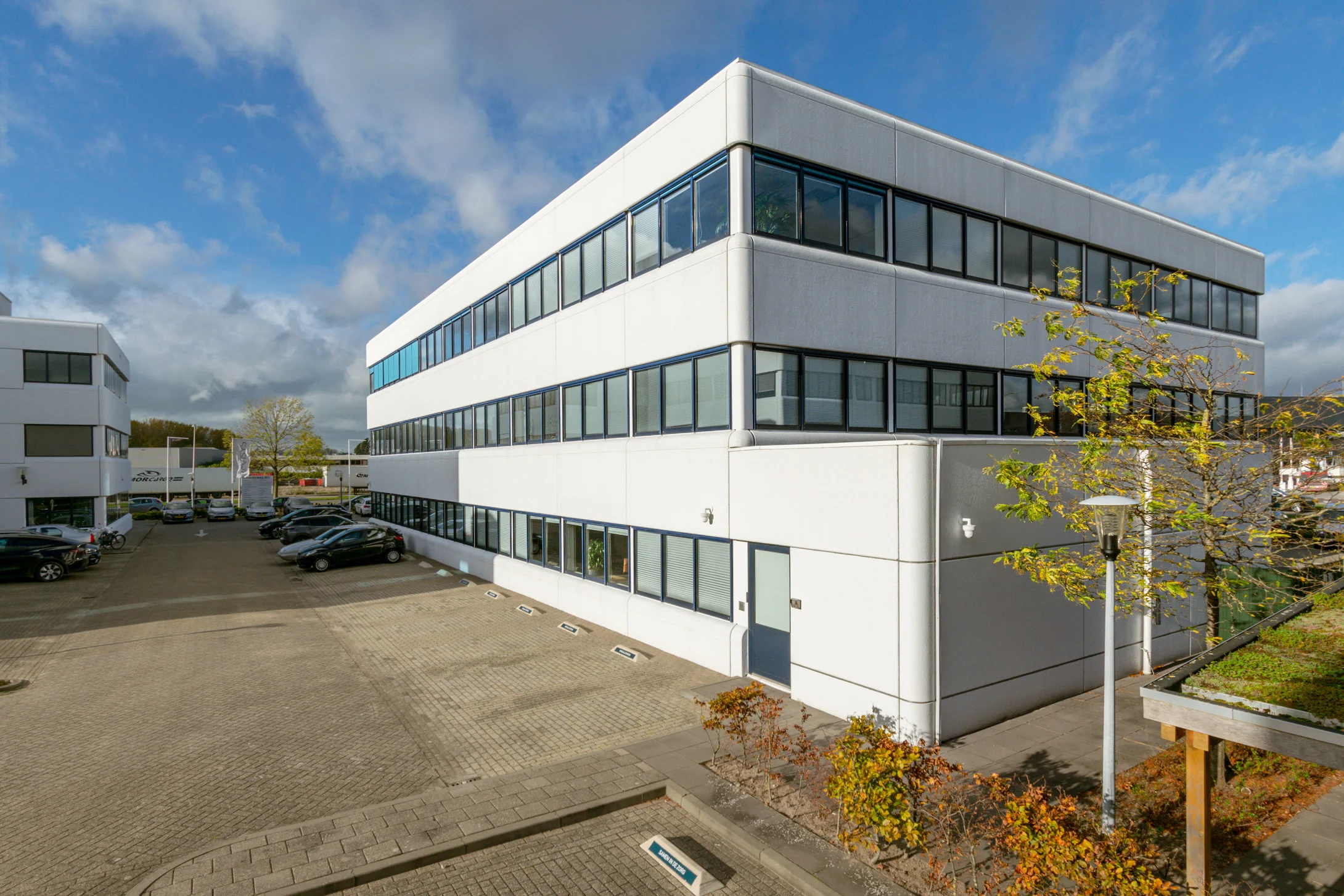 Modern wit kantoorgebouw aan de Atoomweg met parkeerplaatsen en bomen.