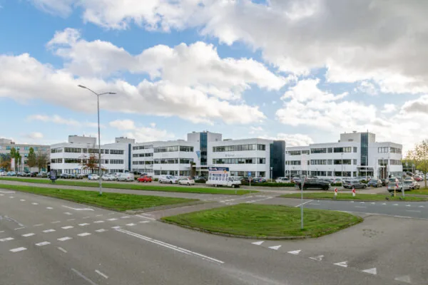 Een modern kantoorgebouw aan de Atoomweg met een drukke parkeerplaats en blauwe lucht op de achtergrond.