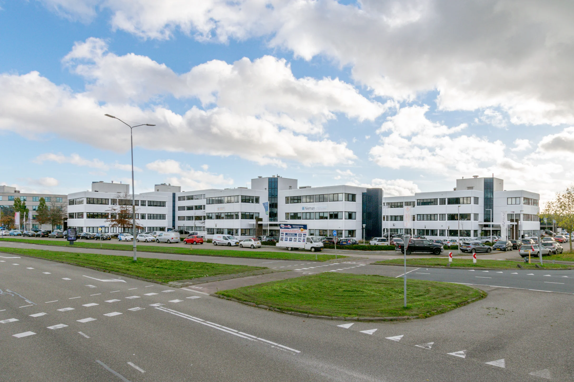 Een modern kantoorgebouw aan de Atoomweg met een drukke parkeerplaats en blauwe lucht op de achtergrond.