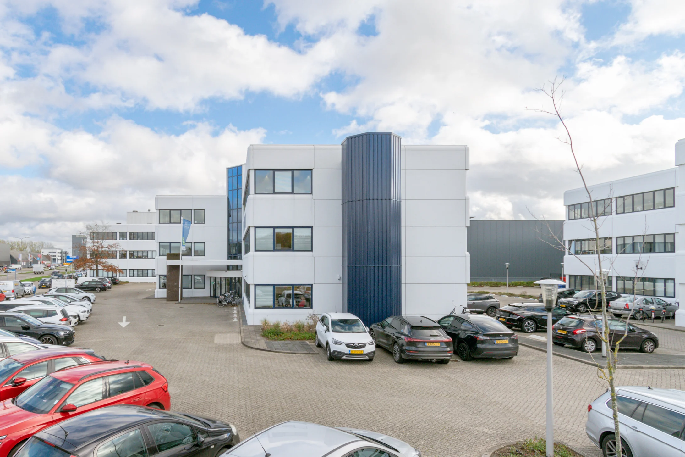 Een modern kantoorgebouw aan de Atoomweg met meerdere geparkeerde auto's ervoor.