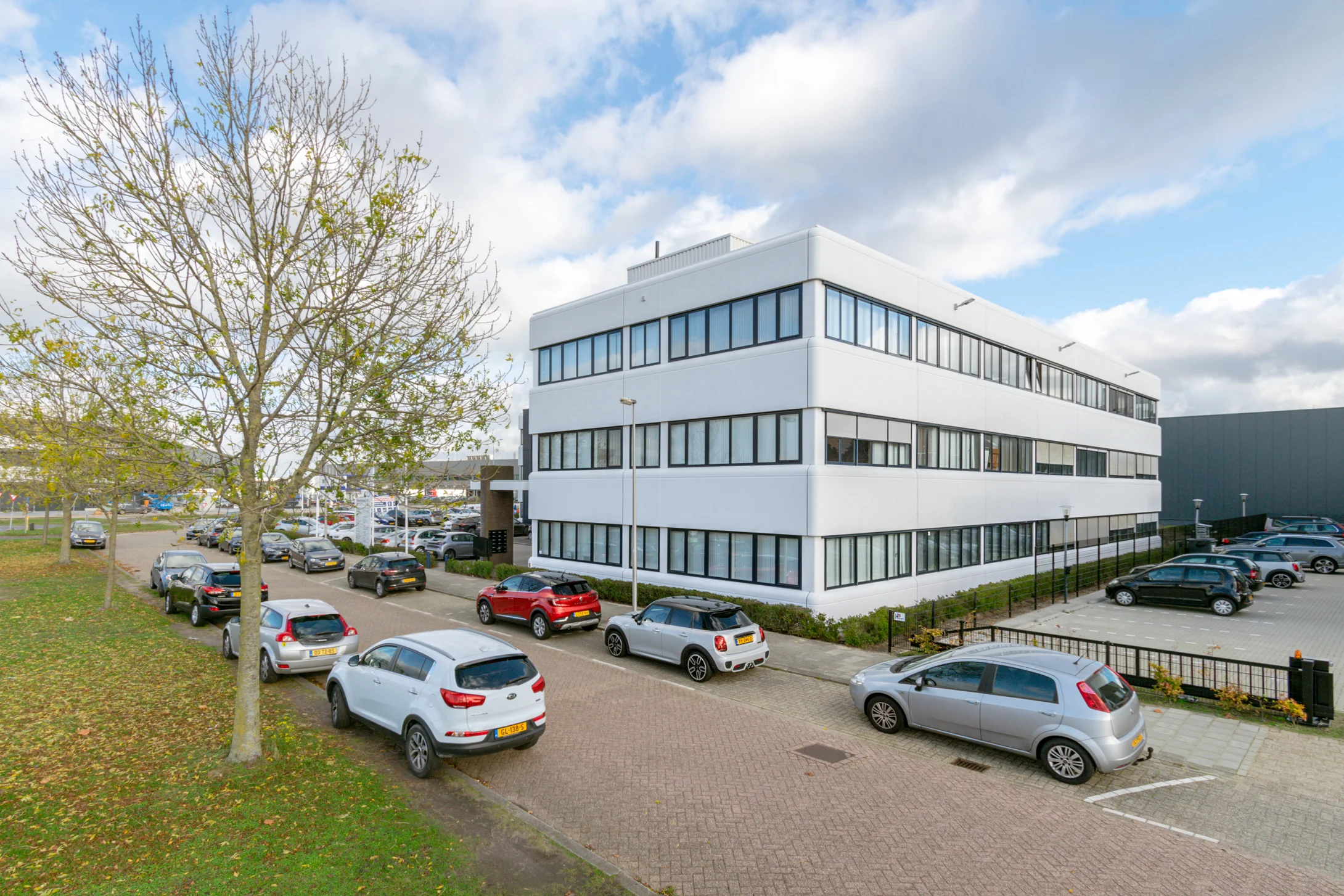 Een modern, wit kantoorgebouw aan de Atoomweg met geparkeerde auto's aan de straatkant.