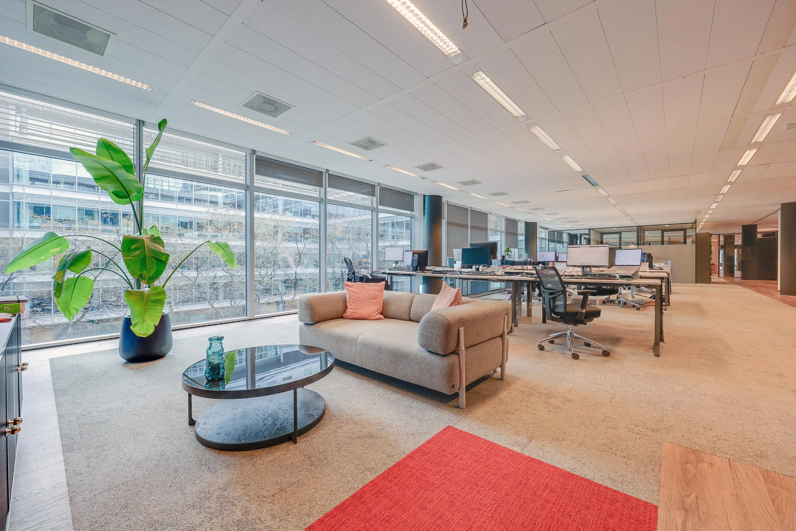 Een moderne kantoorruimte aan de Gustav Mahlerlaan met een bank, planten en bureaus met computers.