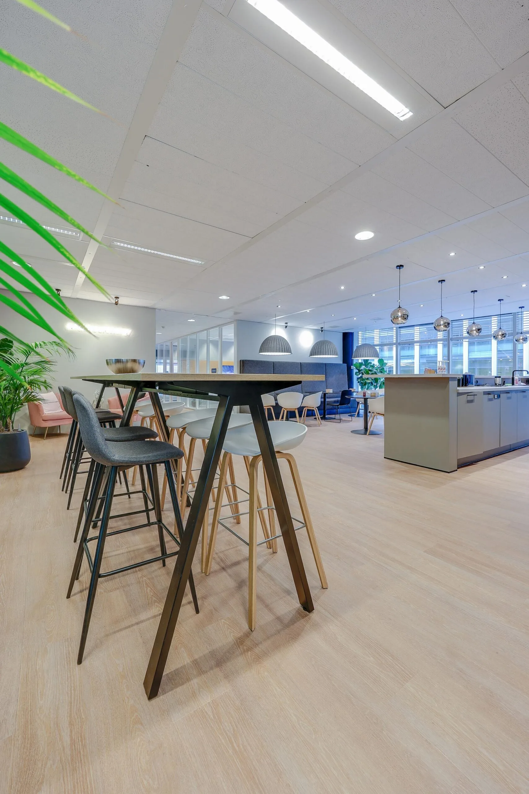 Moderne open kantoorruimte met hoge tafels, barkrukken en hanglampen aan het plafond.
