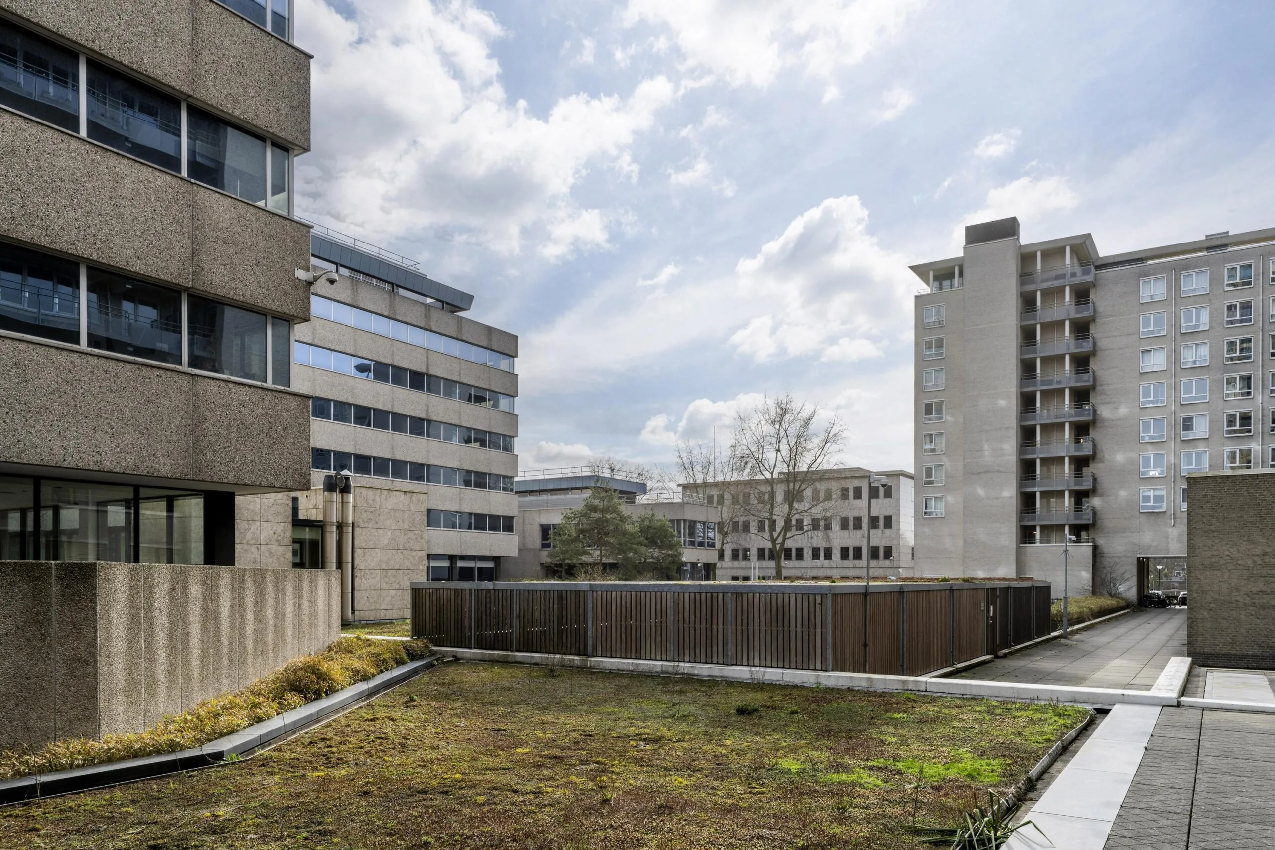 Moderne kantoorgebouwen op Amstelplein met een groen dak en een blauwe lucht.