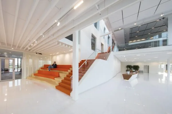 Een moderne, open kantoorruimte met oranje zitplaatsen en een grote trap.