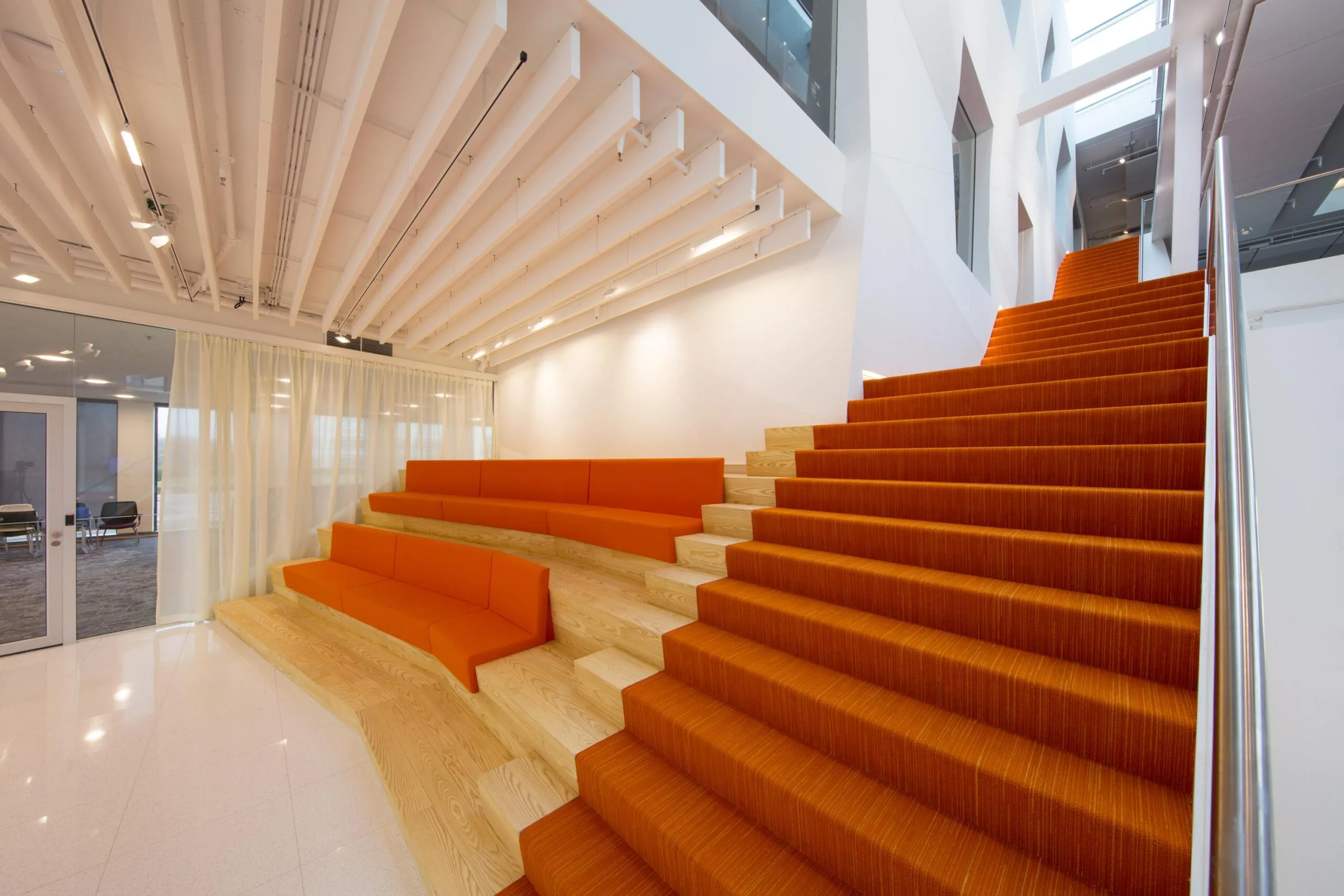 Een modern interieur met houten trappen en oranje zitplaatsen in een open kantoorruimte.