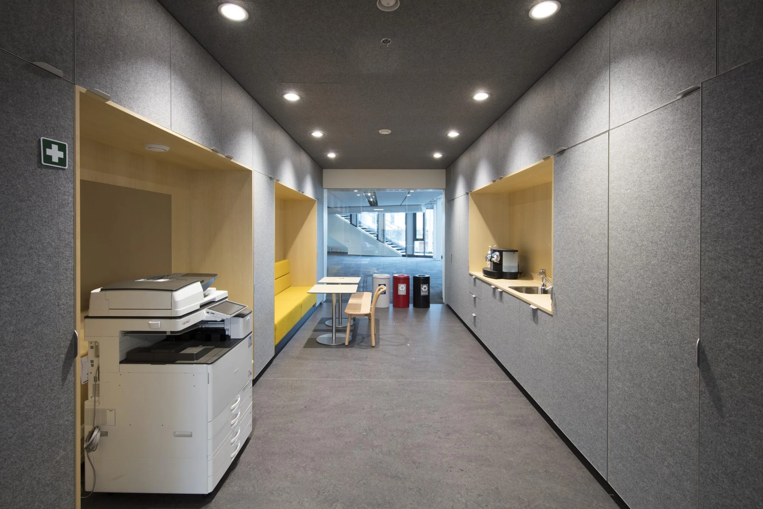 Een moderne gemeenschappelijke ruimte met een printer, zitgedeelte en kitchenette.