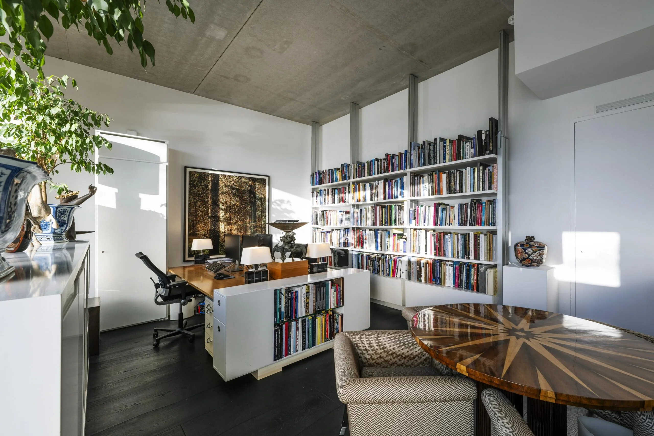 Een strak ingerichte studeerkamer met een houten bureau, boekenplanken en een ronde tafel.