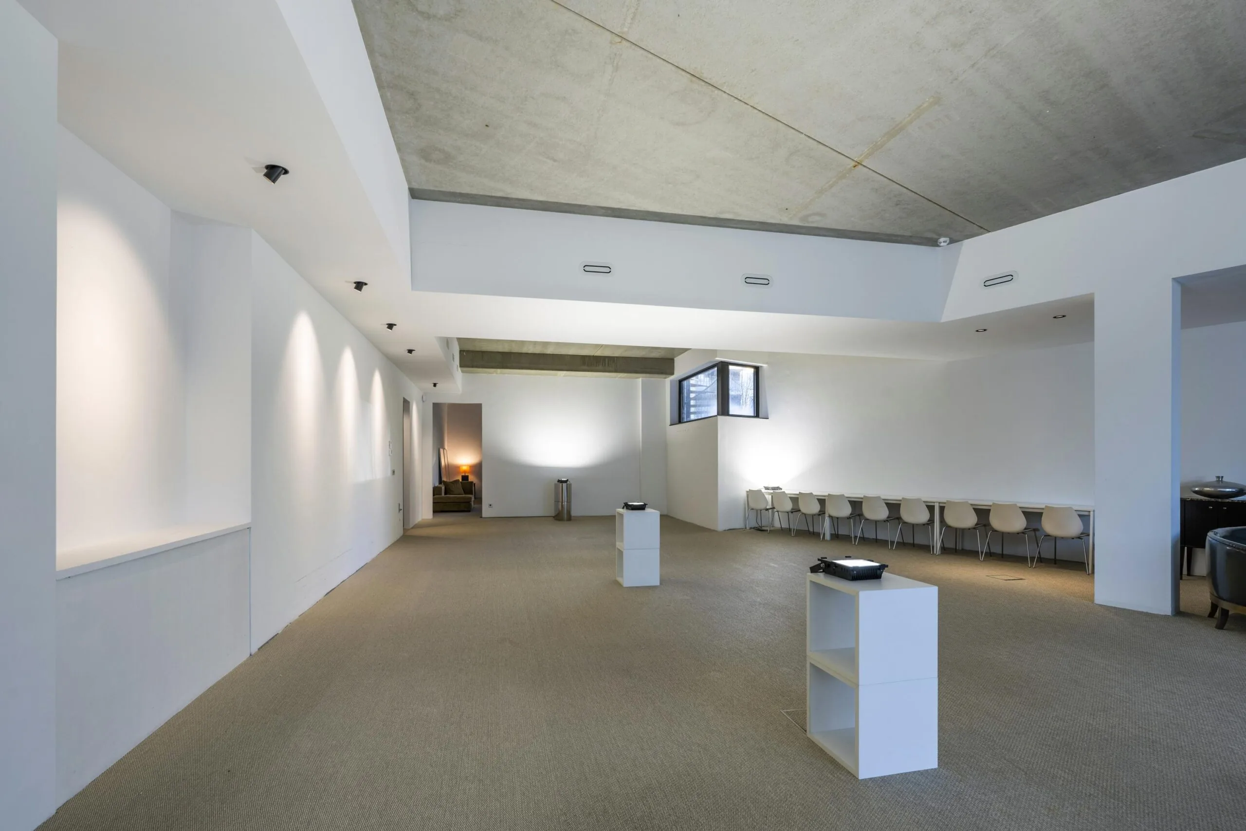 Een ruime, moderne witte kamer met stoelen langs de muur en spotverlichting aan het plafond.