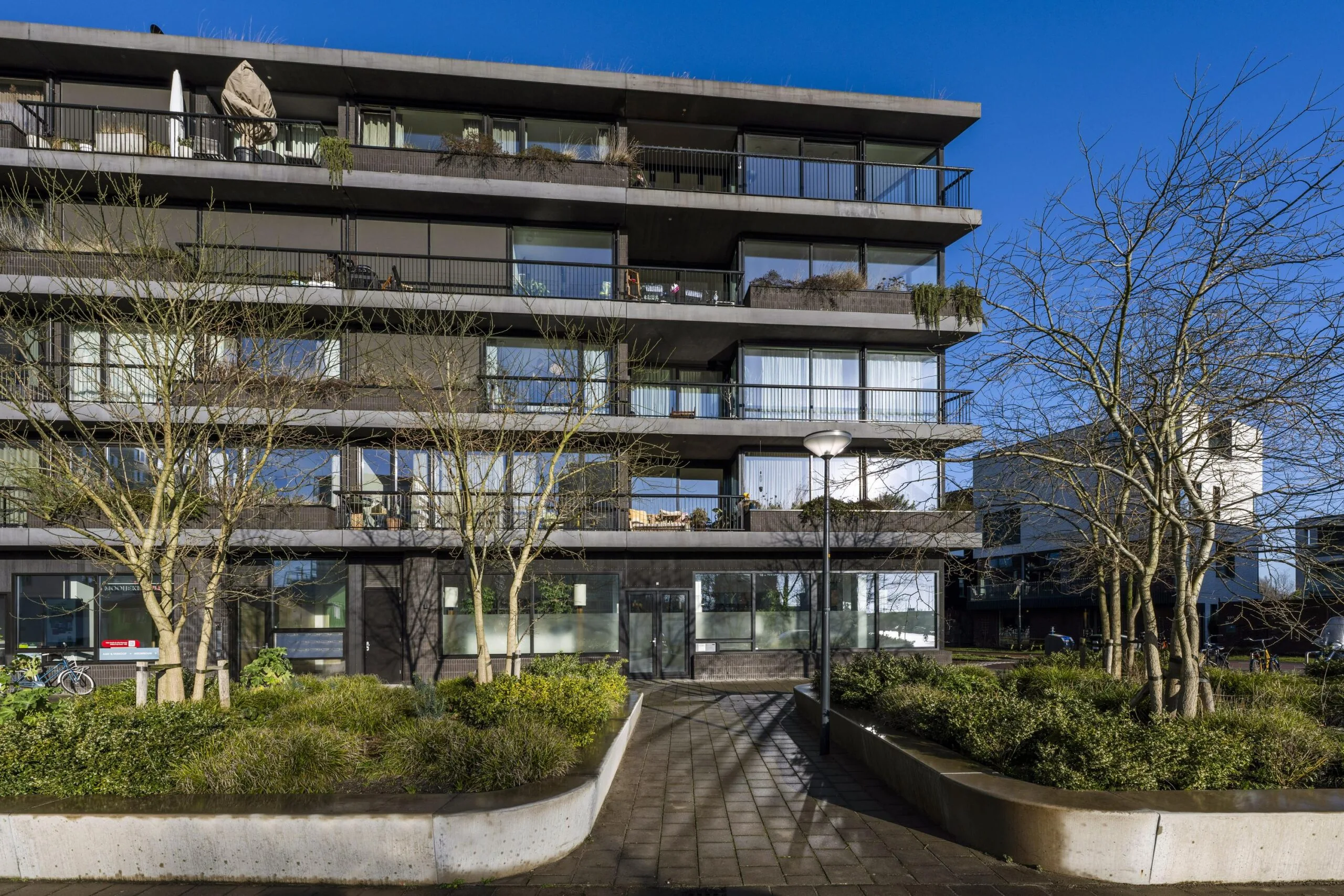 Een modern gebouw met meerdere verdiepingen aan de Lindenhoevestraat, omgeven door bomen en groen.