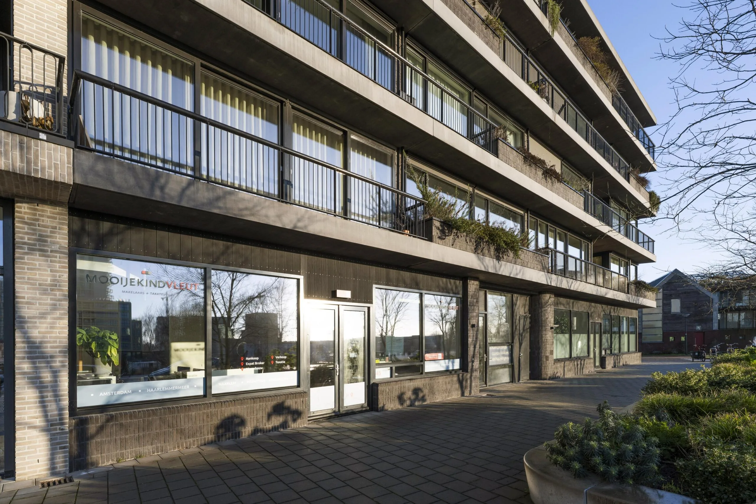 Een modern gebouw met meerdere verdiepingen en een kantoor van Mooijekind Vleut aan de straatkant.