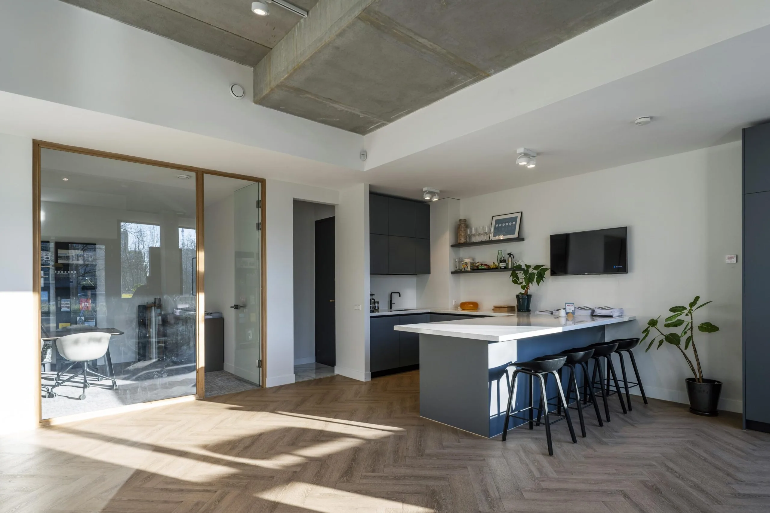 Een moderne keuken met een kookeiland, houten vloer en glazen deur naar een kantoorruimte.