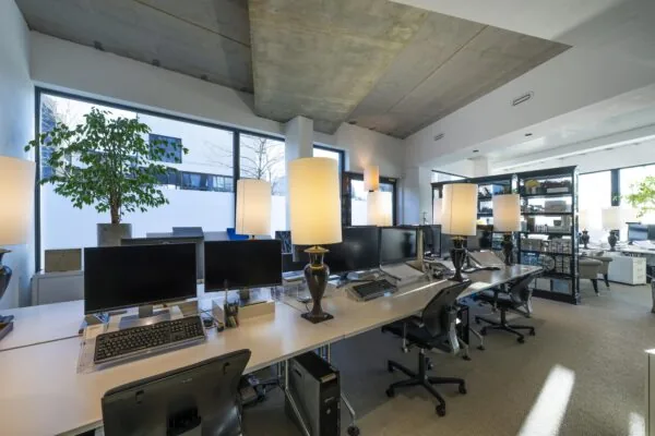 Een modern kantoorinterieur met werkplekken, gloeilampverlichting en buitenzicht door grote ramen.