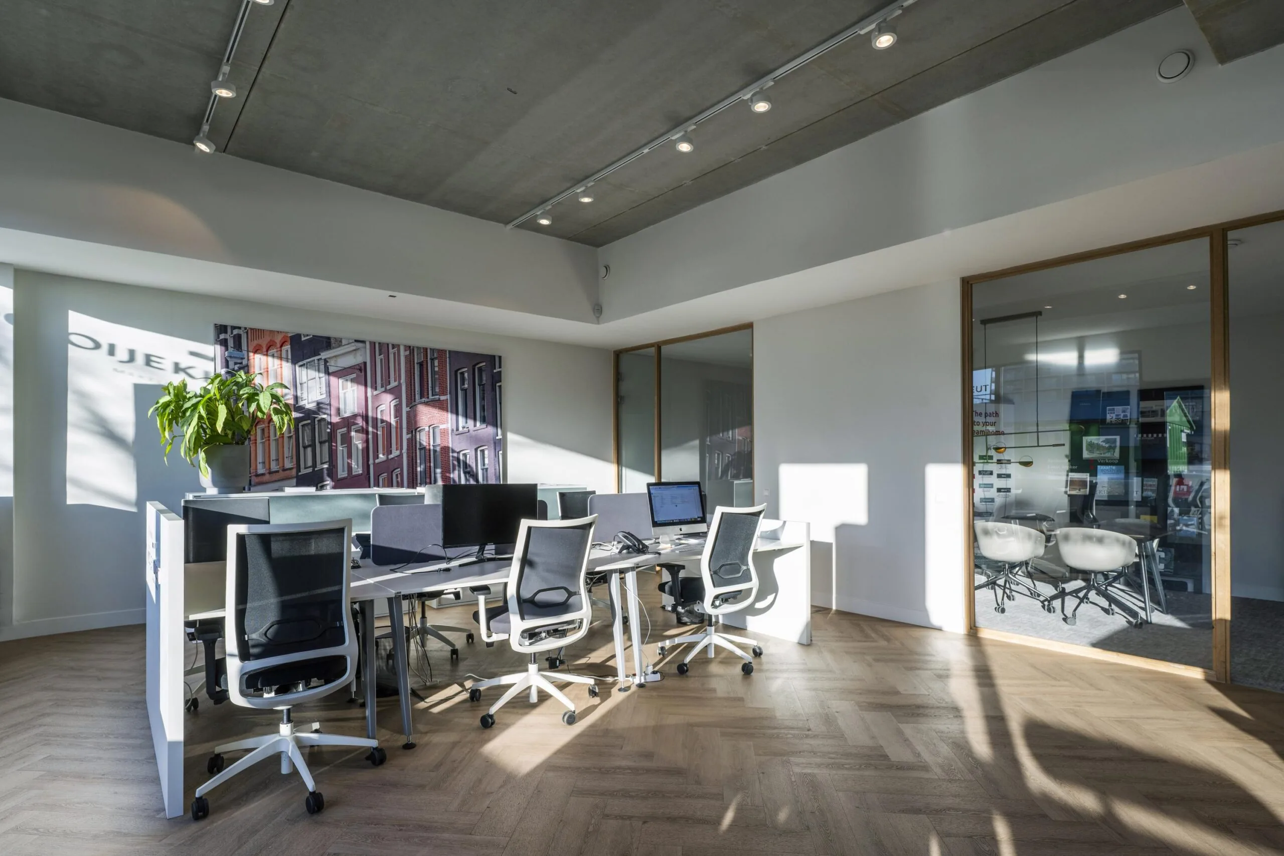 Een moderne kantoorruimte met bureaus, stoelen en een grote afbeelding van een gevel aan de muur.