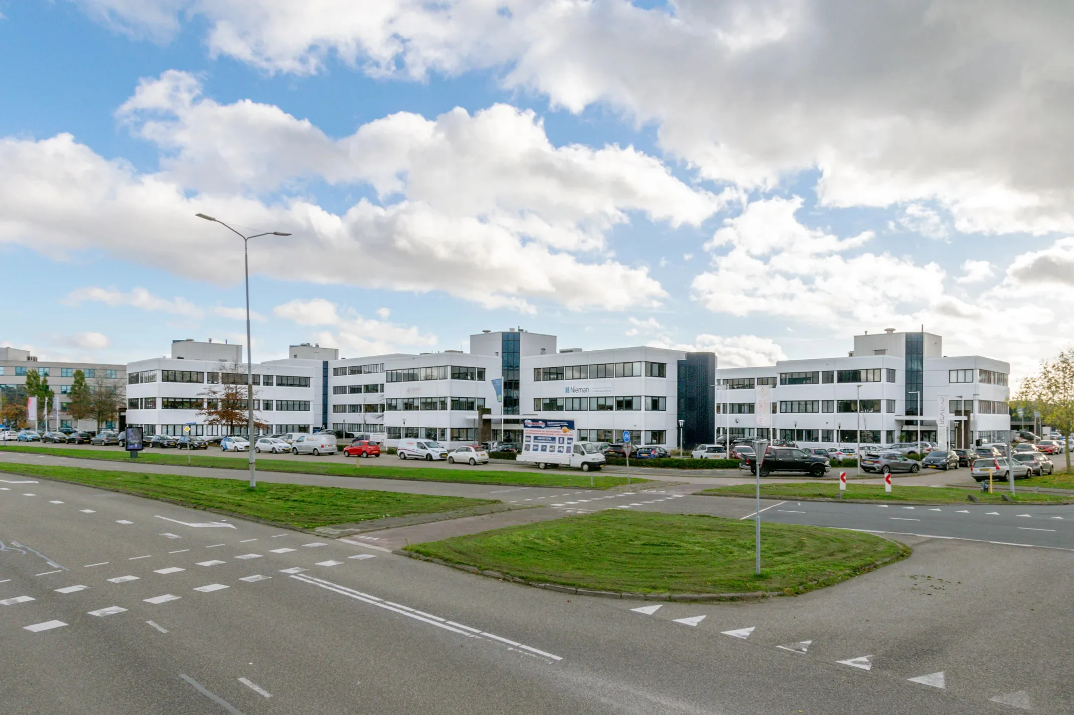 Een modern kantoorgebouw aan de Atoomweg met een groene omgeving en een parkeerplaats op de voorgrond.