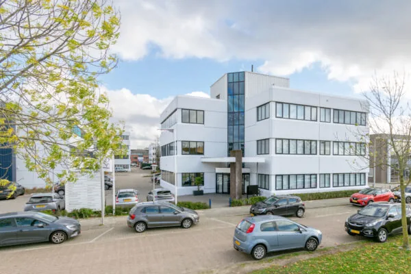 Een modern kantoorgebouw aan de Atoomweg, omringd door geparkeerde auto's en bomen.