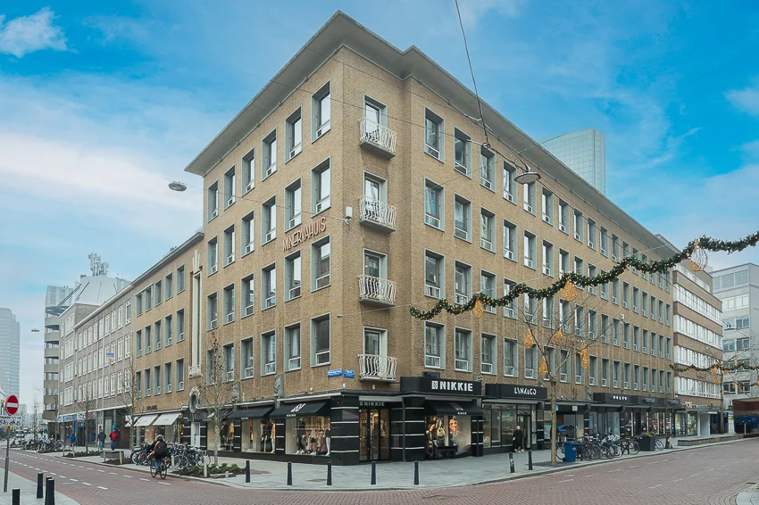 Straatbeeld met het Minervahuis en verschillende winkels op de hoek van de Meent in een stedelijke omgeving.