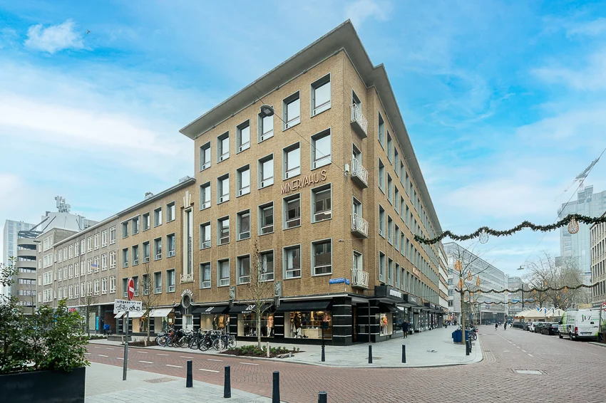 Straatbeeld van het Minervahuis met winkels en fietsenrekken op een zonnige dag.