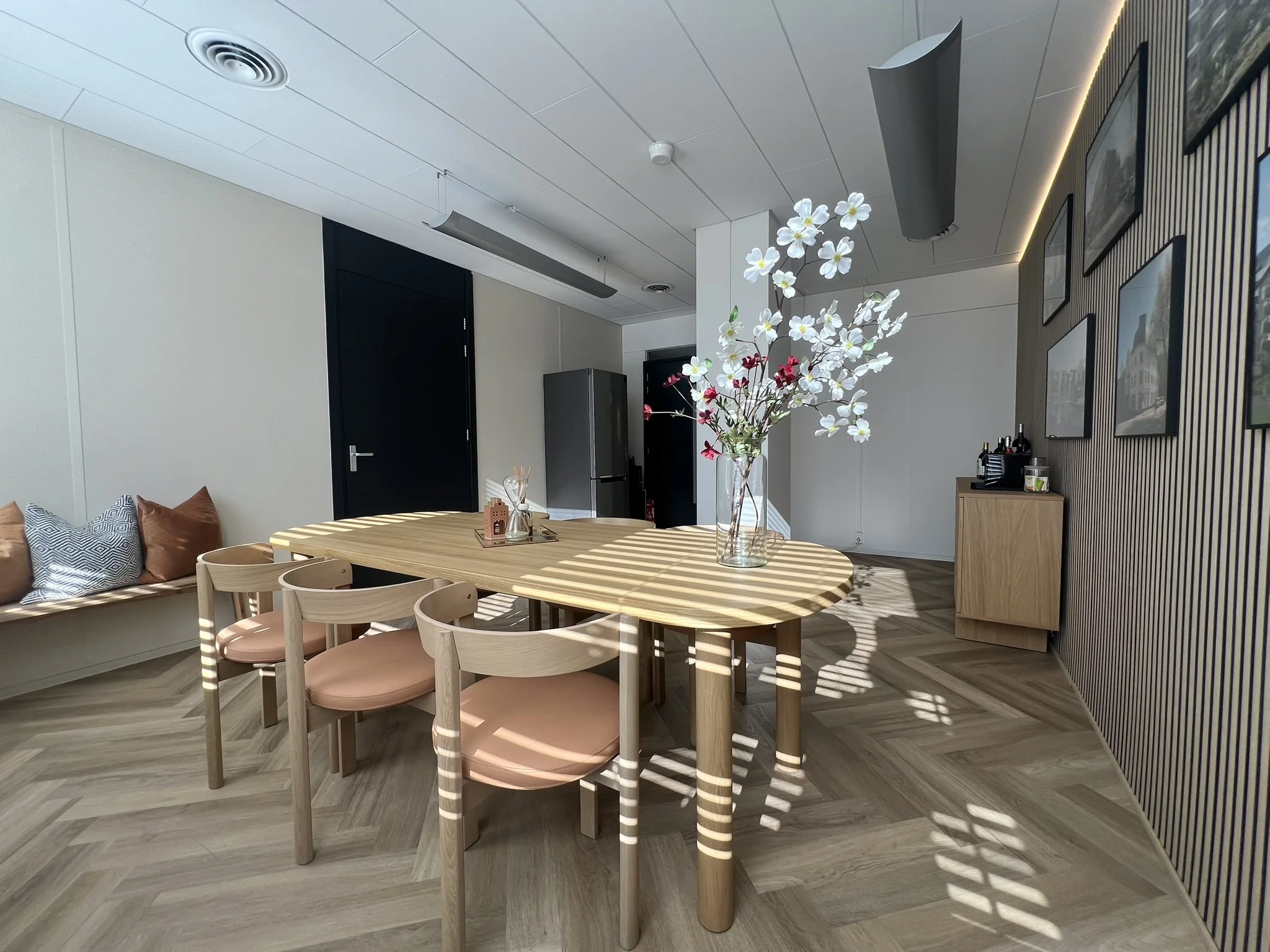 Een moderne eetkamer met een houten tafel, vier stoelen, een vaas met bloemen en strakke decoratie aan de muur.
