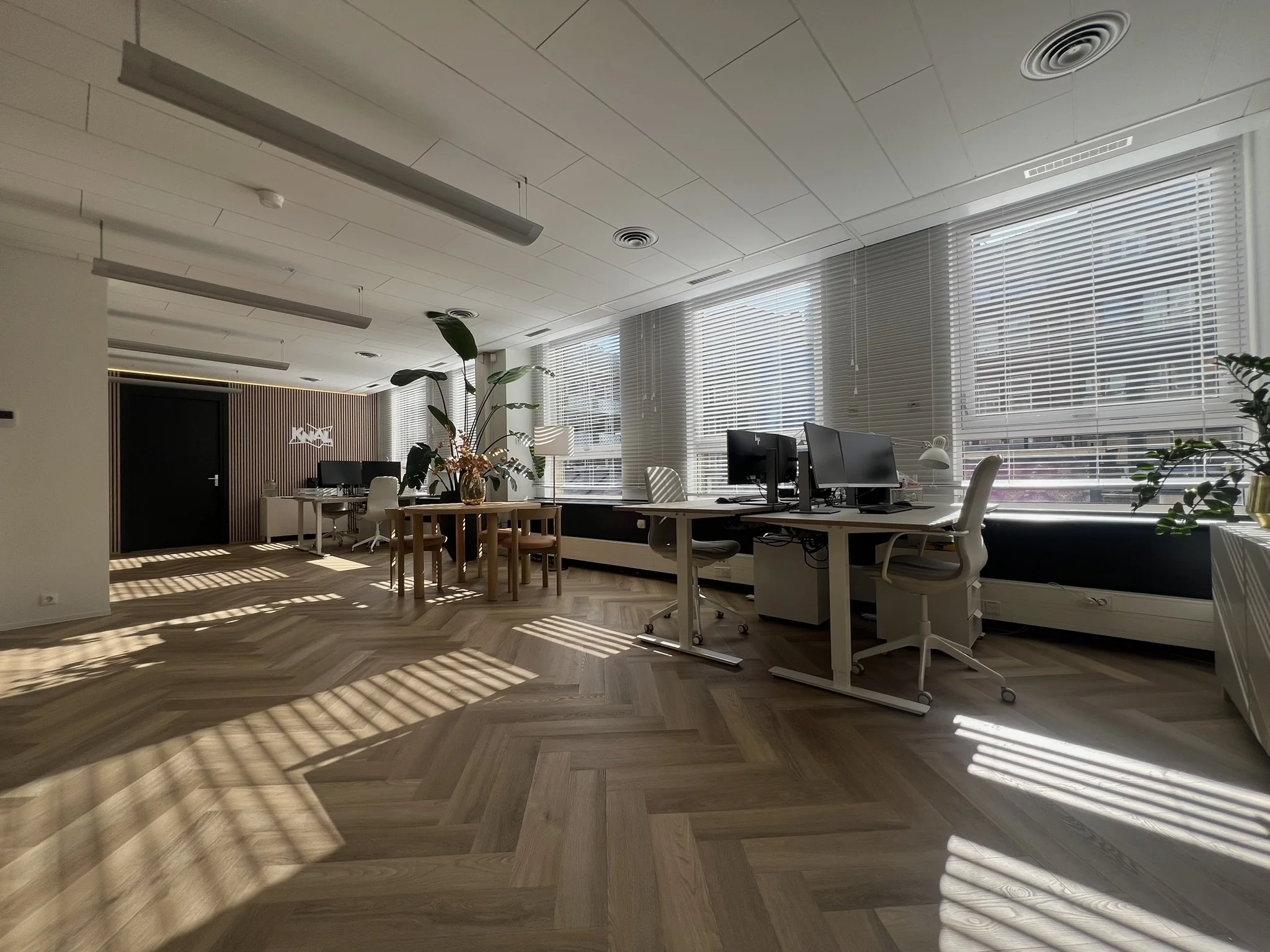Een modern en ruim kantoor met houten vloer en veel natuurlijk licht door jaloezieën.