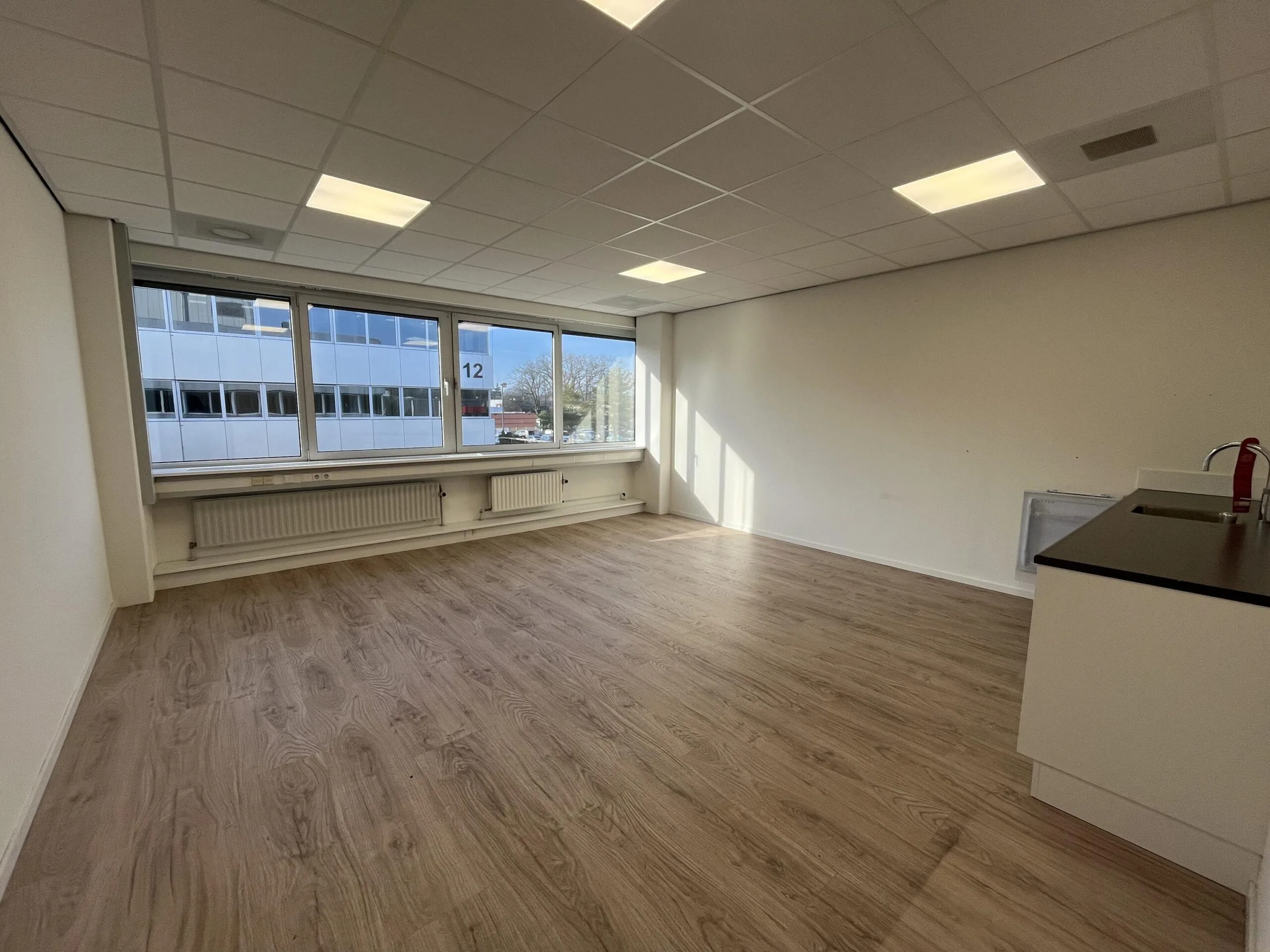Een leeg kantoor met houten vloer en grote ramen aan de Huis-ter-Heideweg.