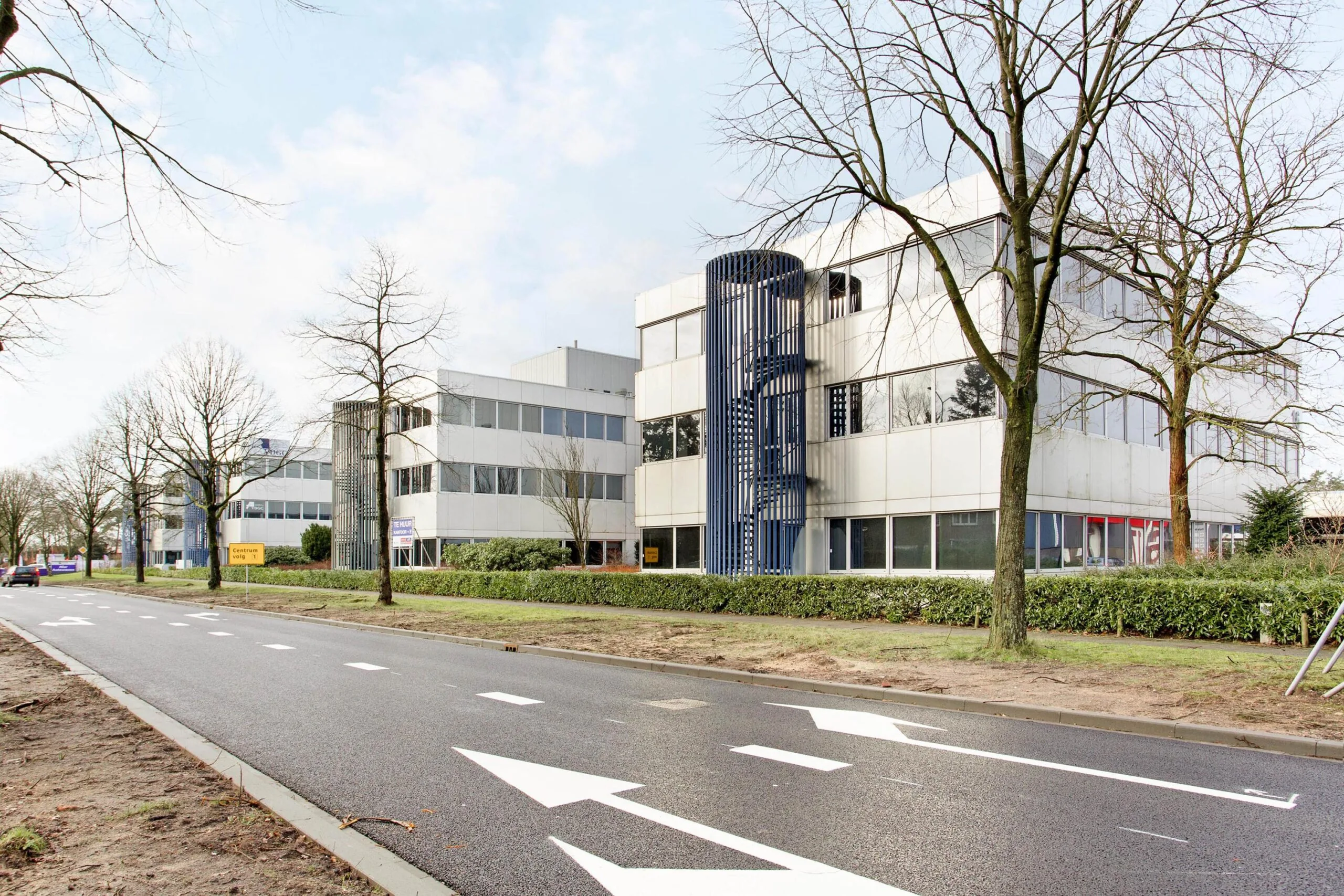 Een modern kantoorgebouw aan de Huis ter Heideweg, omringd door bomen en met duidelijke wegmarkeringen op de voorgrond.