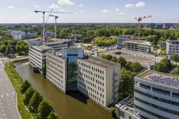 Luchtfoto van moderne kantoorgebouwen aan de Neptunusstraat, omringd door een kanaal en bouwkranen.