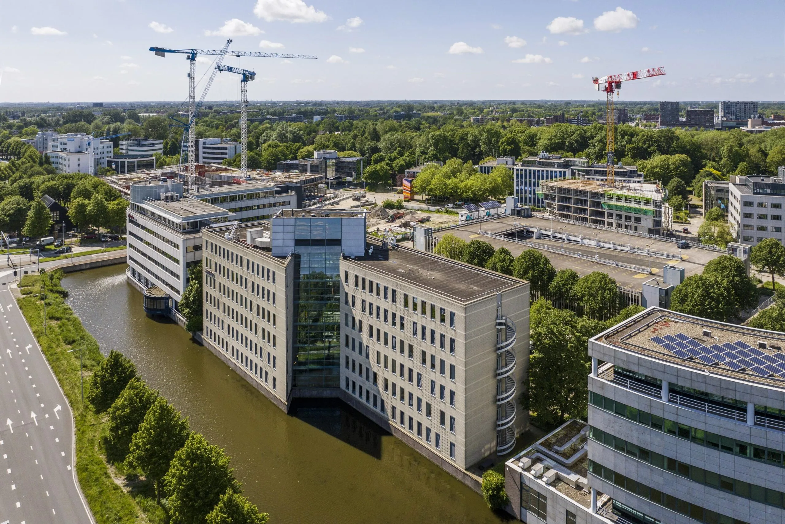 Luchtfoto van moderne kantoorgebouwen aan de Neptunusstraat, omringd door een kanaal en bouwkranen.