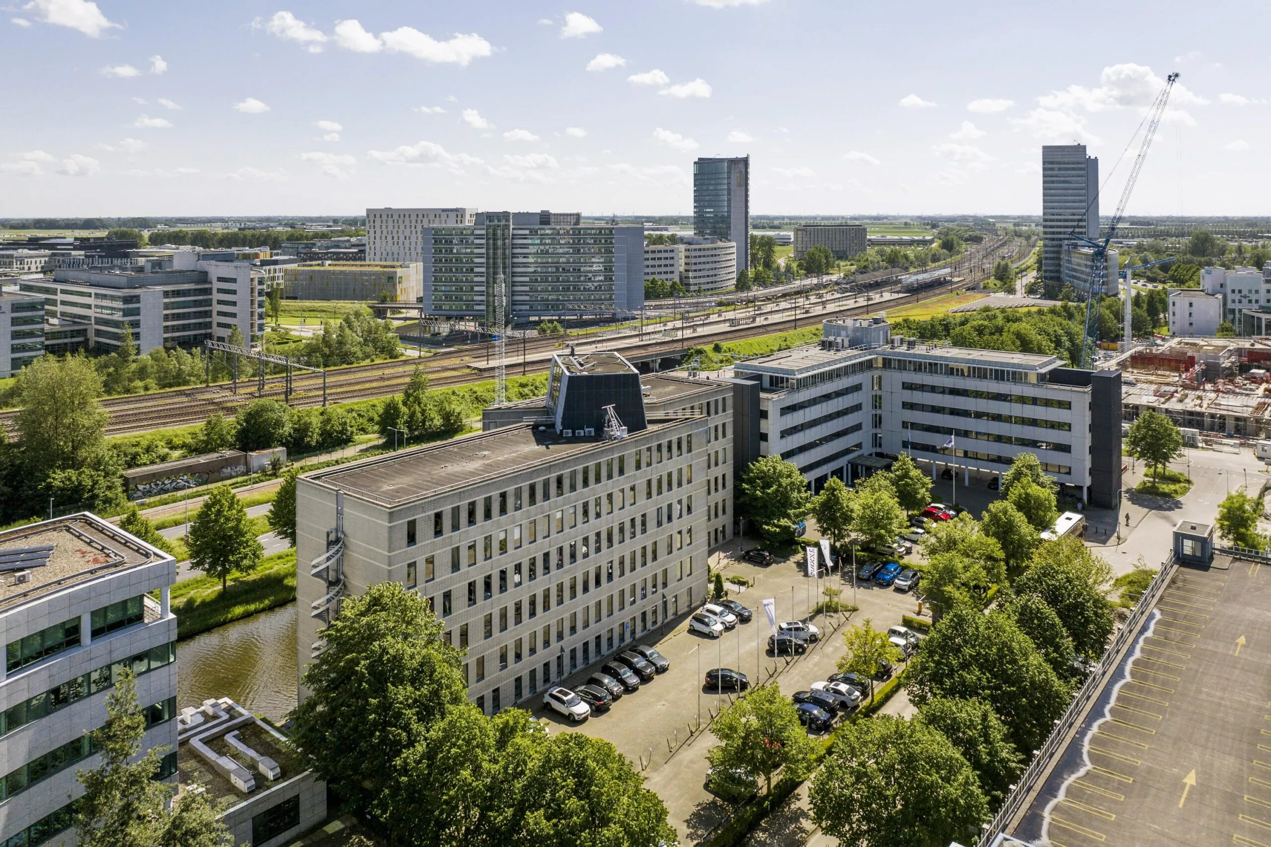 Luchtfoto van kantoorgebouwen en parkeerplaatsen aan de Neptunusstraat, met spoorlijnen en hoogbouw op de achtergrond.